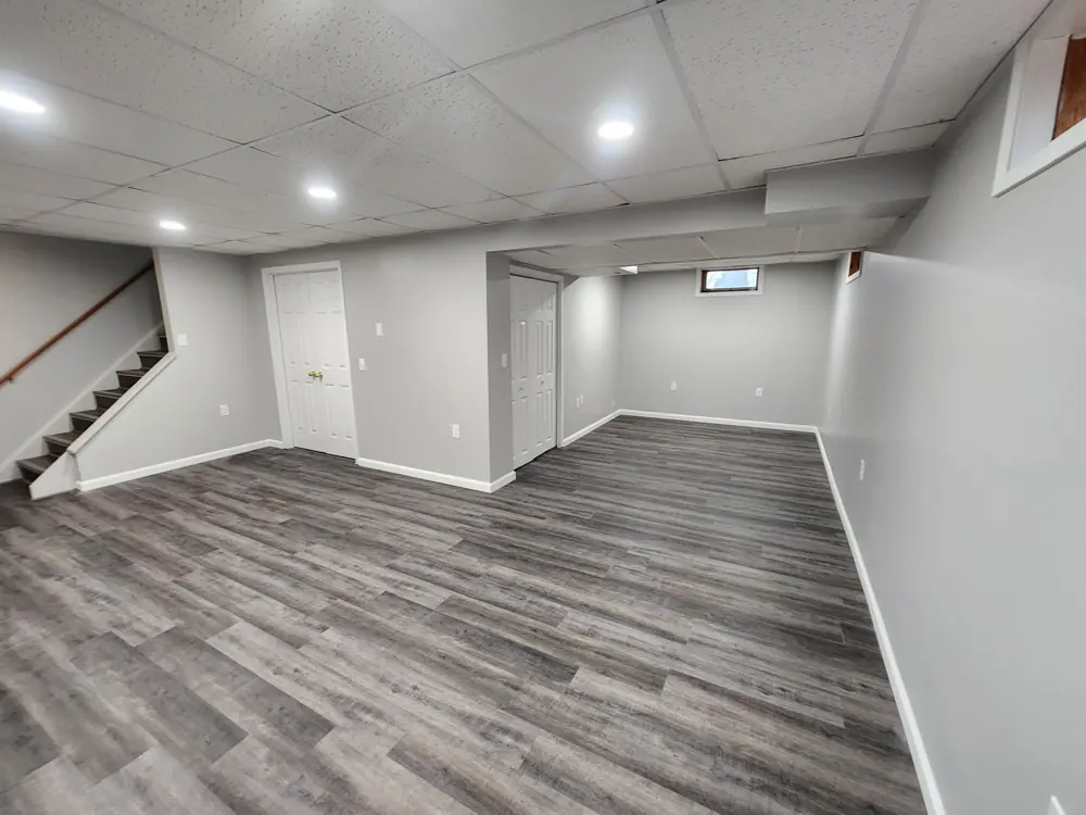 Finished basement with white walls, recessed lighting and grey plank flooring
