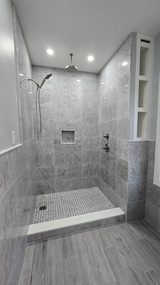 Grey marble-look tiled shower with a pebble floor, a bench and a recessed niche