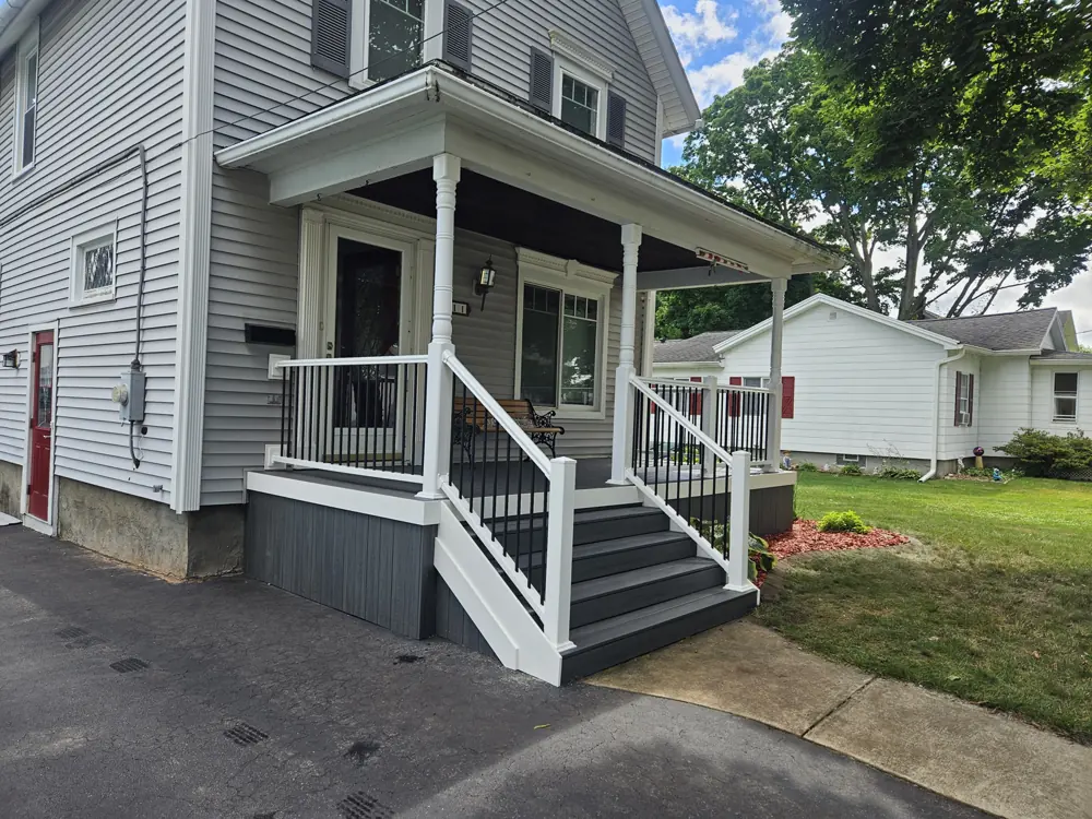 Front porch with white posts, a black railing and steps down to the walk