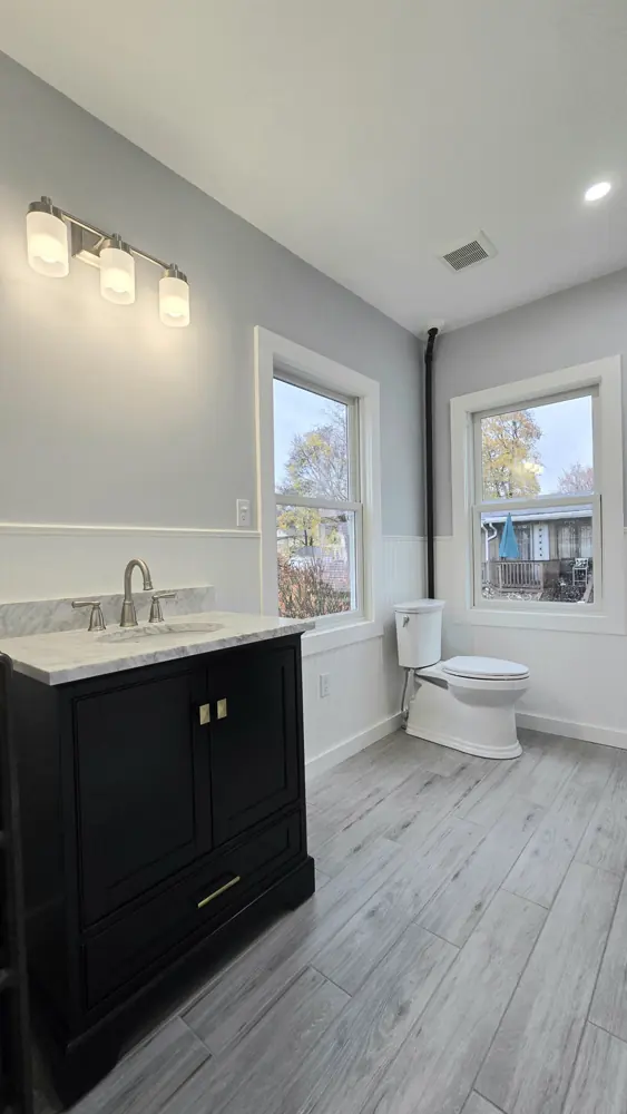 Bathroom vanity with a marble-look top and a dark cabinet beneath two windows