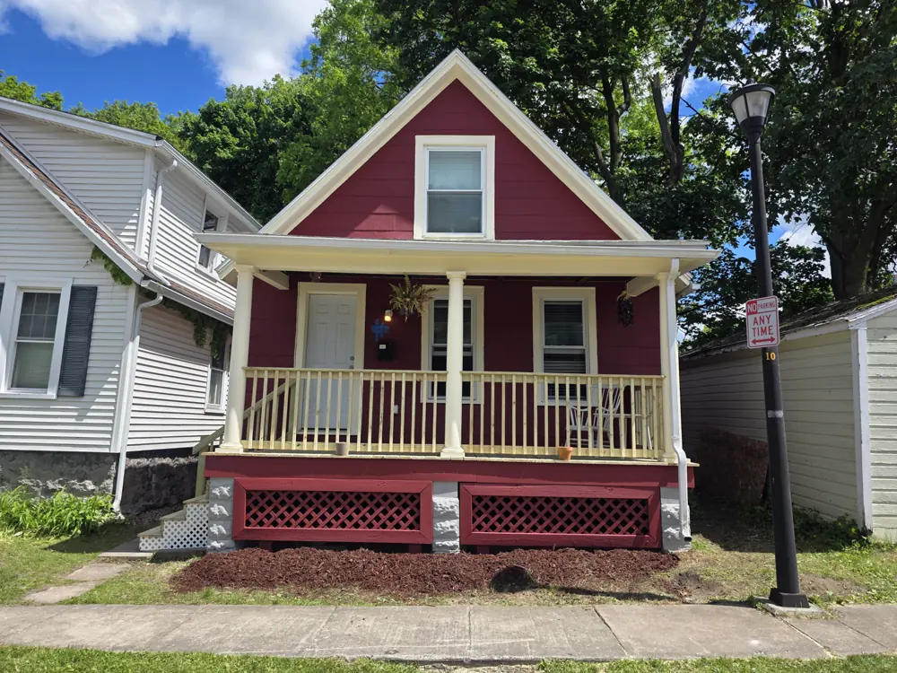 Covered front porch with white railing and lattice skirting on a red house
